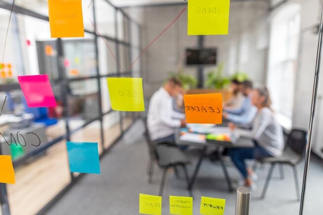 employees in a meeting room seen through a glass door with sticky notes